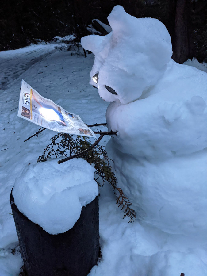 A snow creature reads KP News by flashlight.